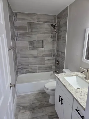 a bathroom with a granite countertop bathtub shower sink vanity and toilet