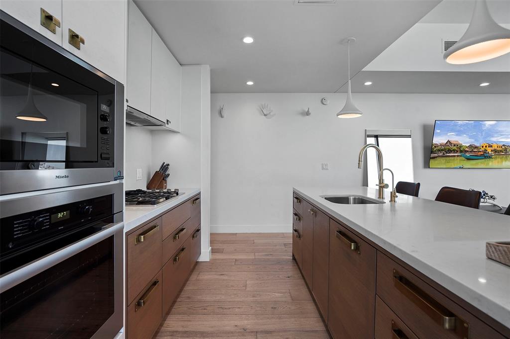 70 Rainey Street, Unit 1409 Austin, TX 78701 - Photo 9 of 38 Dual tone kitchen featuring decorative light fixtures, stainless steel appliances, light wood-style flooring, light stone countertops, and two tone cabinets