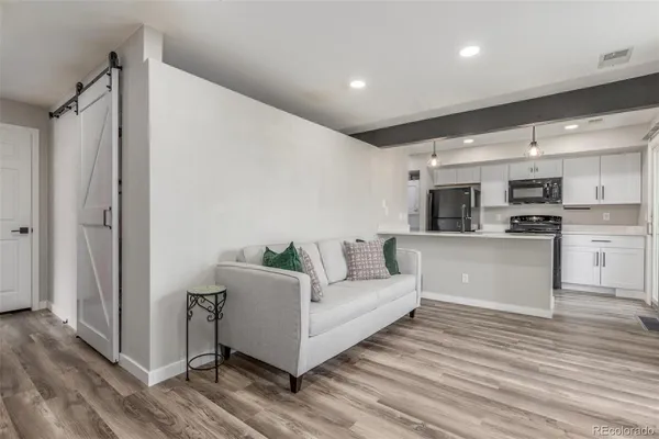 a living room with stainless steel appliances kitchen island granite countertop a refrigerator and a wooden floor