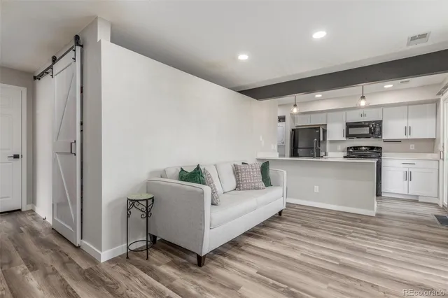 a living room with stainless steel appliances kitchen island granite countertop a refrigerator and a wooden floor