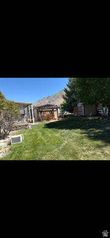 1025 North 300 West, Unit 16 Springville, UT 84663 - Photo 6 of 8 Expansive backyard featuring a manicured lawn, shaded patio area, mature trees, and a mountain backdrop