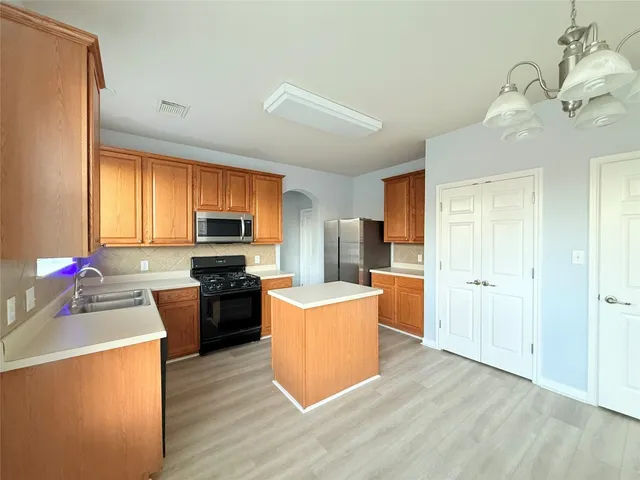 a kitchen with stainless steel appliances a stove a refrigerator a sink dishwasher and wooden cabinets with wooden floor