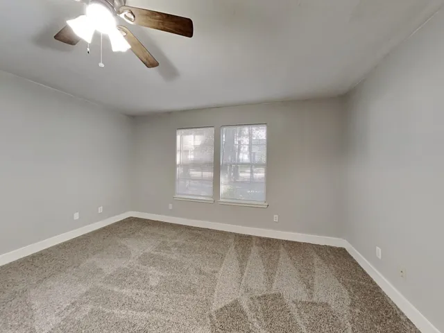 an empty room with a chandelier fan and windows