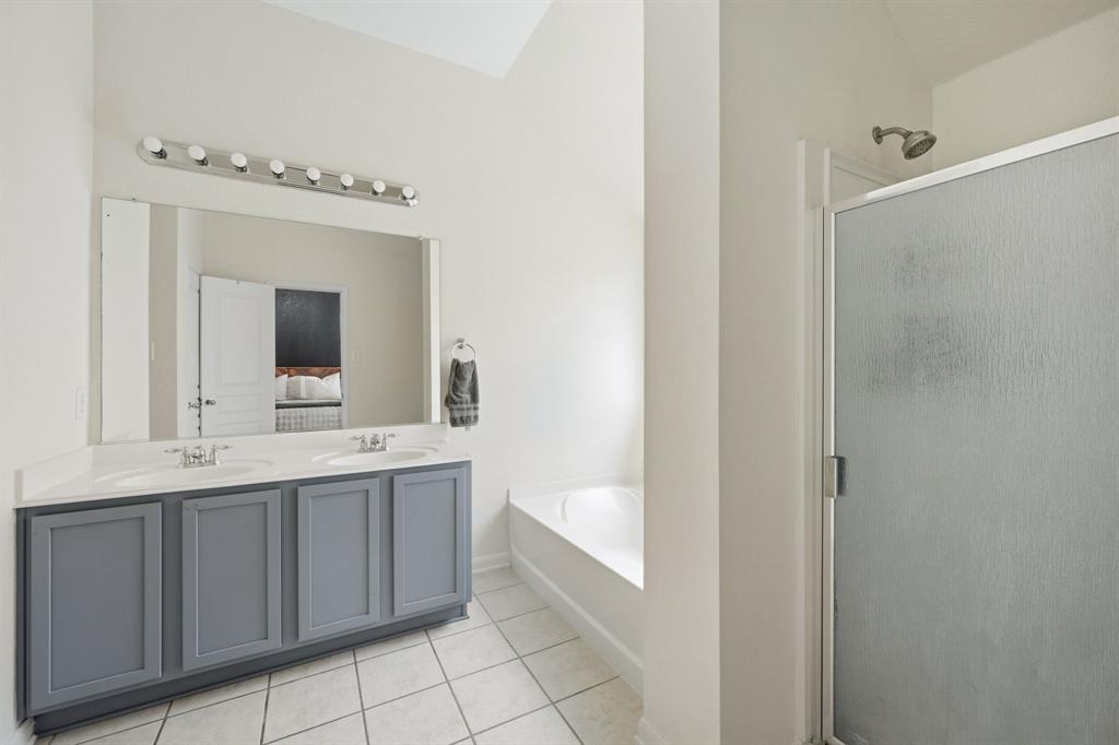 14152 Rodeo Daze Drive Fort Worth, TX 76052 - Photo 16 of 20 Bathroom featuring a double vanity with gray cabinetry and white countertops, a large mirror, a chrome light fixture, a built-in bathtub, and a separate shower with a frosted glass enclosure