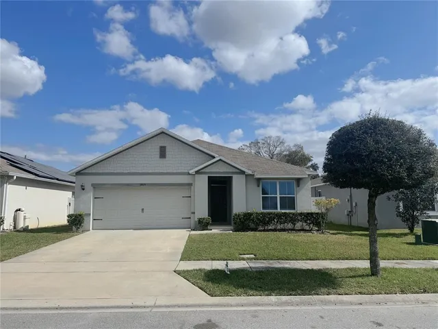a view of a big house in front of a big yard with plants and large tree