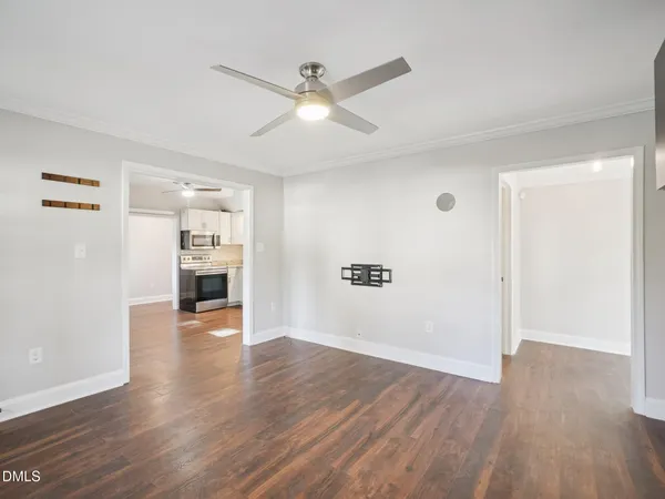 an empty room with wooden floor a ceiling fan and kitchen view