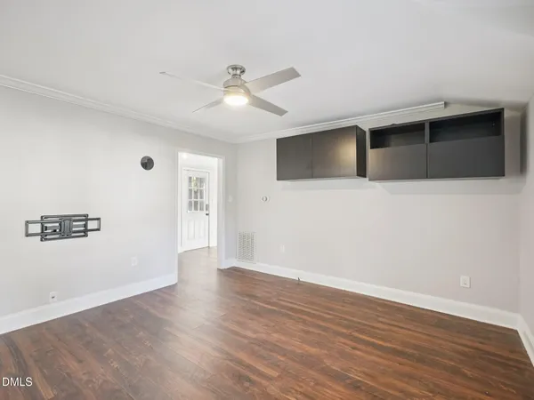 a view of an empty room with wooden floor and a ceiling fan