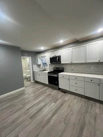 a kitchen with stainless steel appliances granite countertop a stove top oven a sink dishwasher and white cabinets with wooden floor