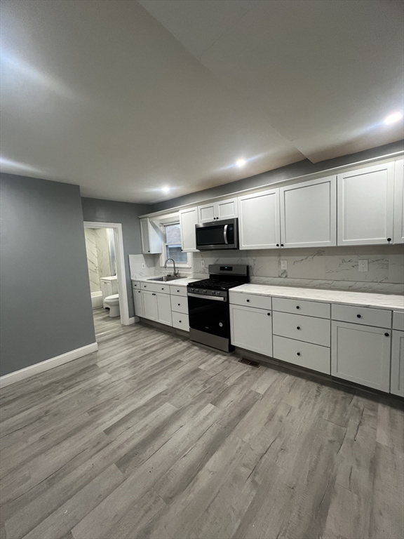 10 Essex Street, Unit 1 Brockton, MA 02301 - Photo 2 of 10 a kitchen with stainless steel appliances granite countertop a stove top oven a sink dishwasher and white cabinets with wooden floor