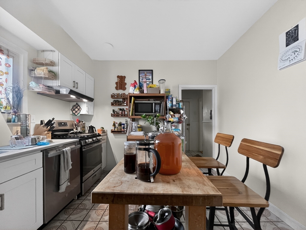 49 Porter Street Somerville, MA 02143 - Photo 5 of 40 a kitchen with stainless steel appliances granite countertop a stove top oven a dining table and chairs with wooden floor