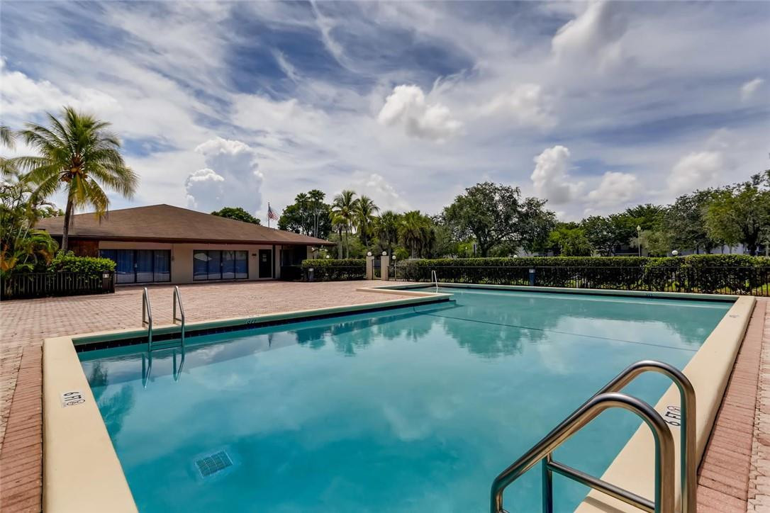 9763 West McNab Road, Unit 214 Tamarac, FL 33321 - Photo 27 of 28 a view of a swimming pool with a table and chairs under an umbrella