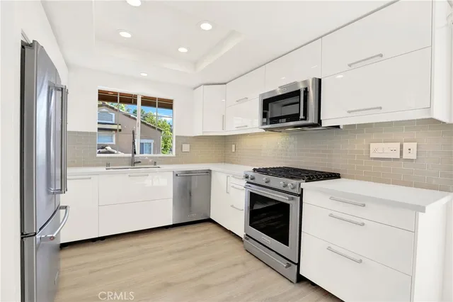 a kitchen with stainless steel appliances granite countertop white cabinets a sink a stove a microwave and a refrigerator