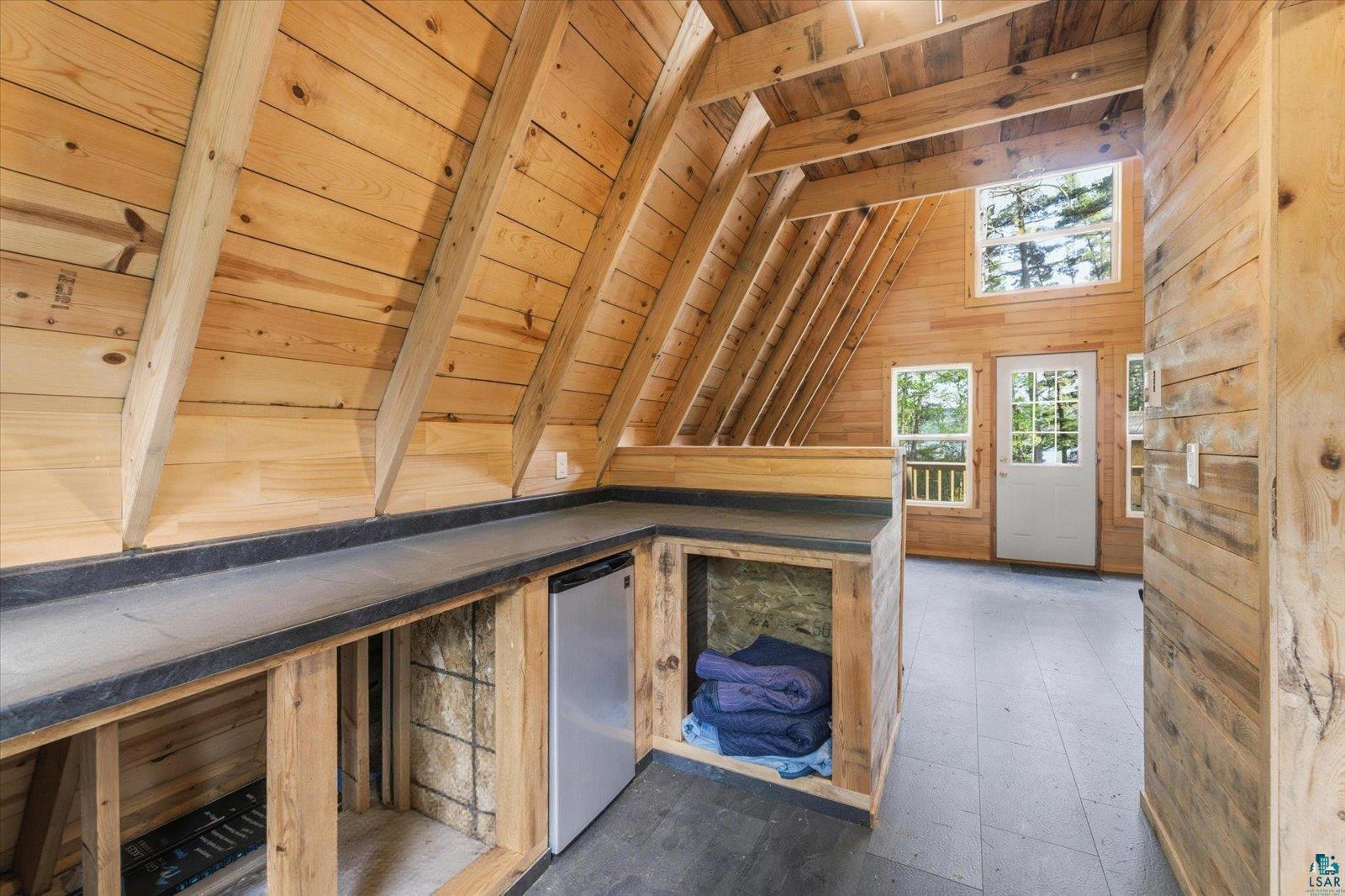 5298 Long Island Tower, MN 55790 - Photo 22 of 31 Open-concept room featuring exposed timber framing, natural wood-paneled walls and ceiling, slate-finish flooring, and a built-in counter with a compact refrigerator