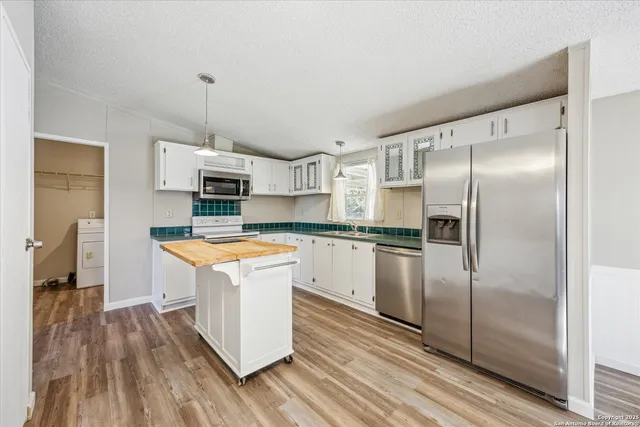 a kitchen with stainless steel appliances granite countertop a refrigerator a sink dishwasher a stove and white countertops with wooden floor