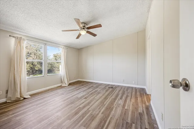 a view of empty room with wooden floor and fan