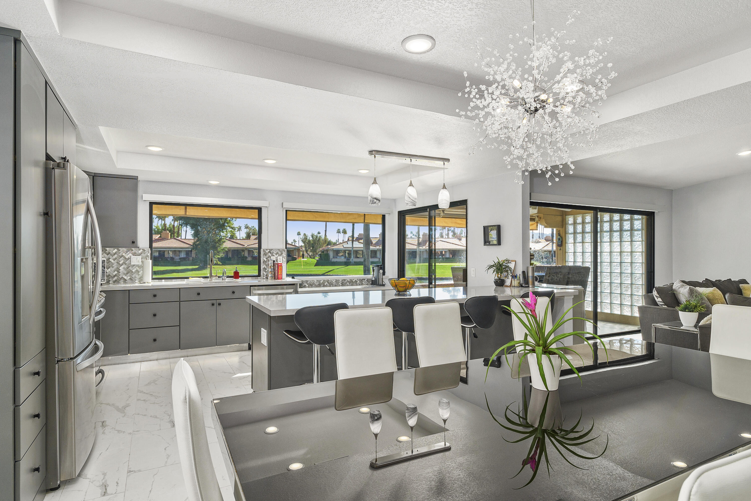 43 Conejo Circle Palm Desert, CA 92260 - Photo 13 of 58 a room with lots of white furniture a chandelier a potted plant and a large window