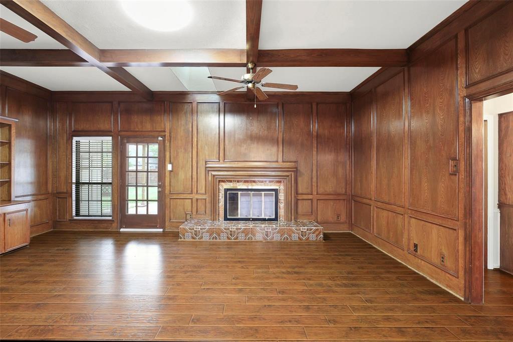 10135 Rita Road Dallas, TX 75243 - Photo 11 of 24 Unfurnished living room featuring ceiling fan, coffered ceiling, wood walls, a glass covered fireplace, and dark wood-type flooring