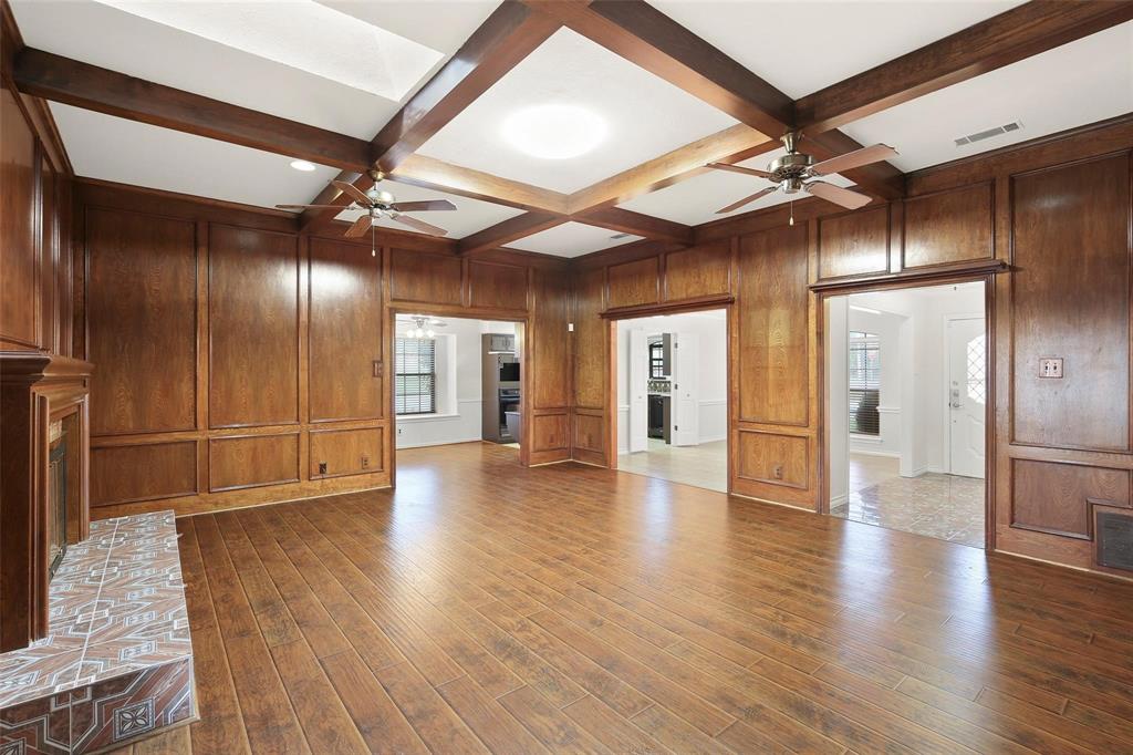 10135 Rita Road Dallas, TX 75243 - Photo 9 of 24 Unfurnished living room featuring coffered ceiling, a fireplace with raised hearth, ceiling fan, dark wood-style floors, and wood walls