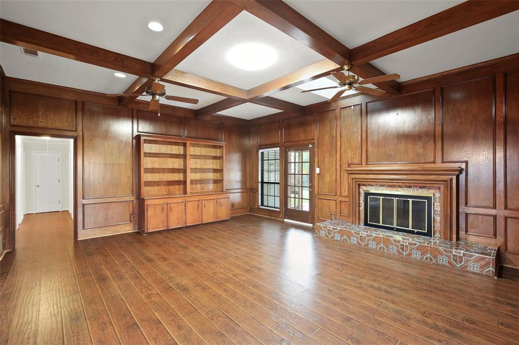 10135 Rita Road Dallas, TX 75243 - Photo 10 of 24 Unfurnished living room featuring wood walls, coffered ceiling, a ceiling fan, dark wood finished floors, and a glass covered fireplace