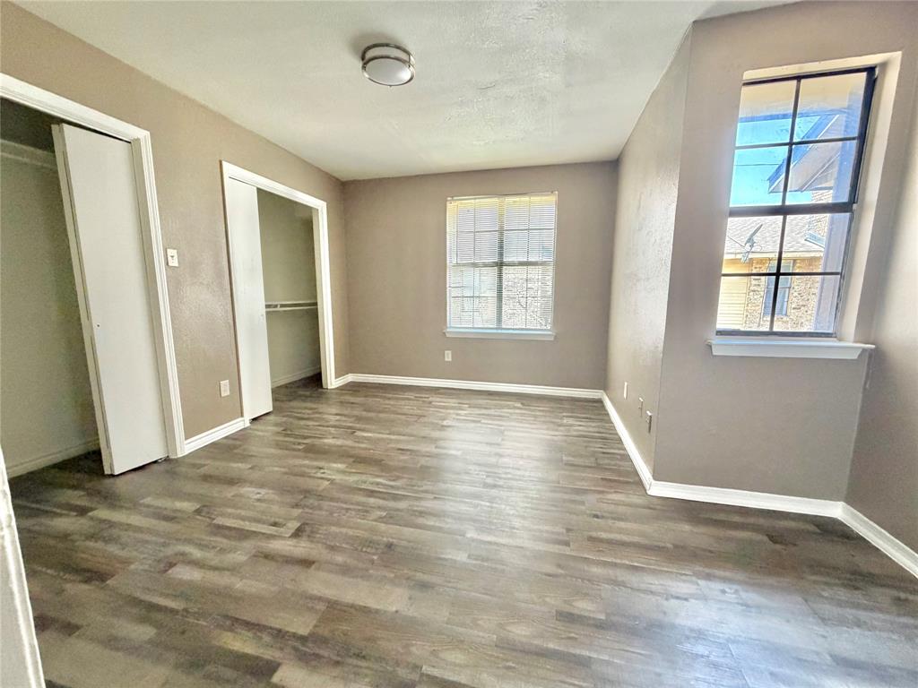 8001 Rothington Road, Unit 33 Dallas, TX 75227 - Photo 11 of 15 Spacious room featuring wood-finish flooring, two windows with white trim, a flush-mount ceiling light fixture, and two built-in closet spaces with bi-fold doors
