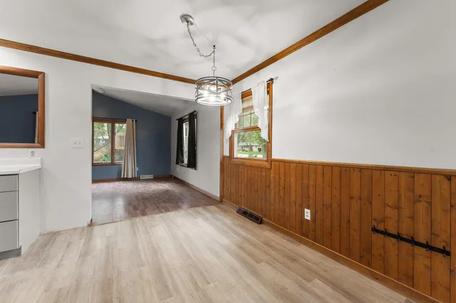 an empty room with wooden floor chandelier and windows