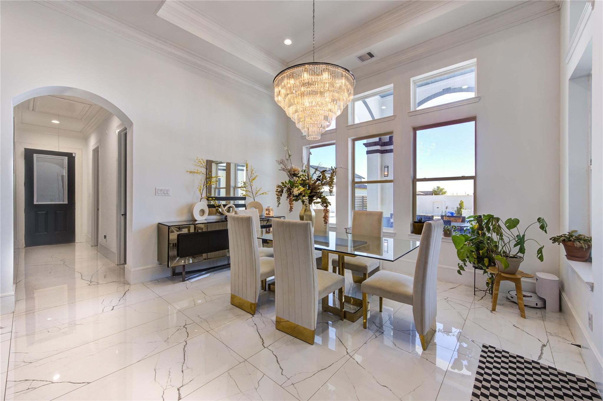 4821 Walters Road Richmond, TX 77469 - Photo 30 of 50 This elegant formal dining room exudes modern luxury with soaring tray ceilings, oversized windows, and a breathtaking multi-tier crystal chandelier serving as the centerpiece of the space. The sleek glass dining table, designer seating with gold accents, and polished marble-style flooring create a sophisticated atmosphere ideal for upscale entertaining. Filled with natural light and finished with refined contemporary touches
