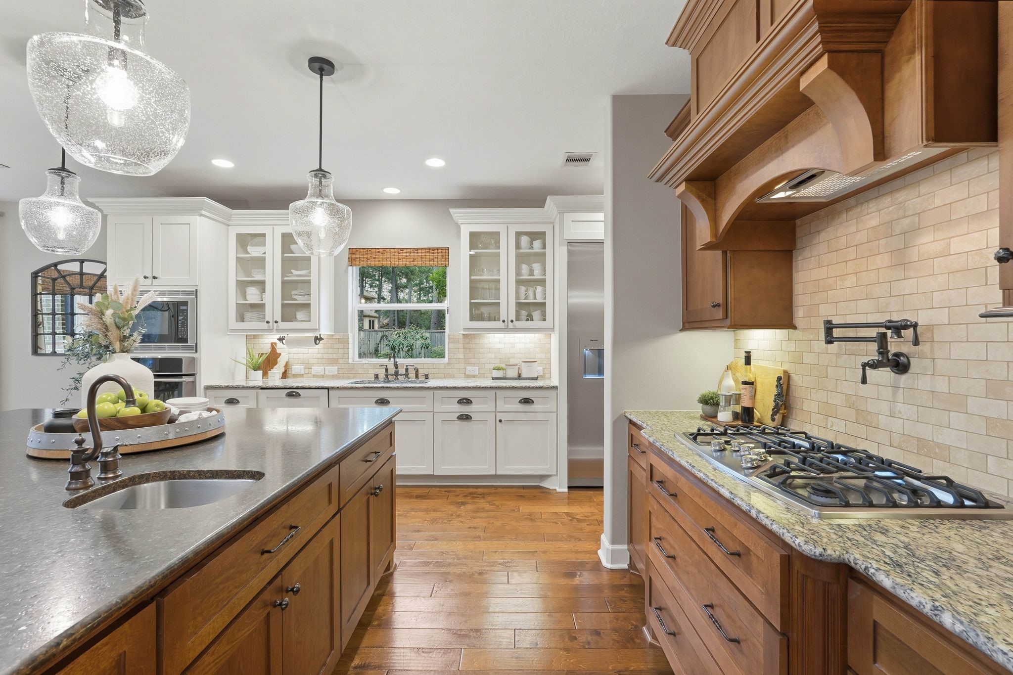 147 West Valera Ridge Place The Woodlands, TX 77389 - Photo 16 of 50 Chef’s kitchen featuring a gas cooktop with pot filler, custom vent hood, deep pots-and-pans drawers, oversized island with prep sink, granite countertops, and designer pendant lighting.