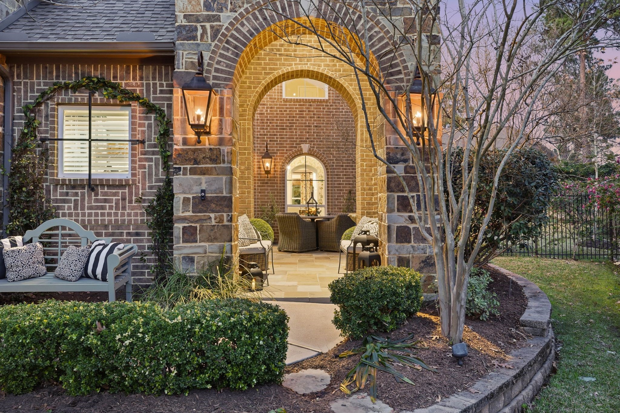 147 West Valera Ridge Place The Woodlands, TX 77389 - Photo 3 of 50 Architectural courtyard entrance with a dramatic arched stone walkway, brick detailing, and gas exterior lighting. Manicured landscaping and a cozy sitting area create a refined and welcoming first impression.