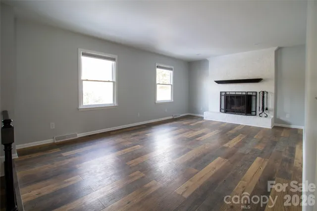an empty room with wooden floor fireplace and windows