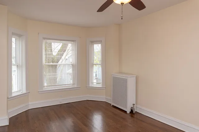an empty room with wooden floor chandelier fan and windows