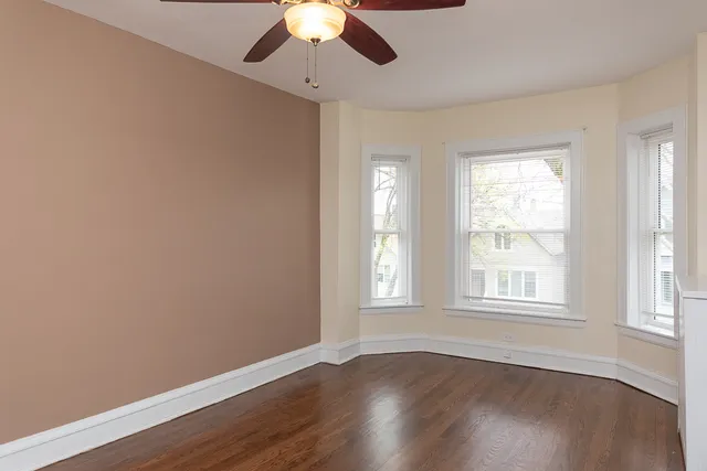 an empty room with wooden floor chandelier fan and windows