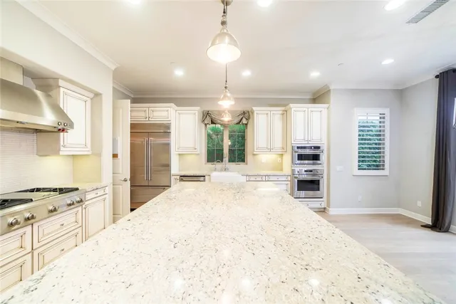 a large white kitchen with granite countertop a stove a sink a refrigerator and white cabinets with wooden floor