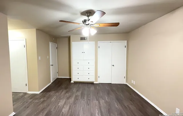 an empty room with wooden floor closet fan and windows