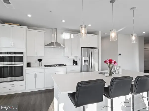 a kitchen with stainless steel appliances kitchen island granite countertop a refrigerator a stove top oven a sink dishwasher and white cabinets with wooden floor