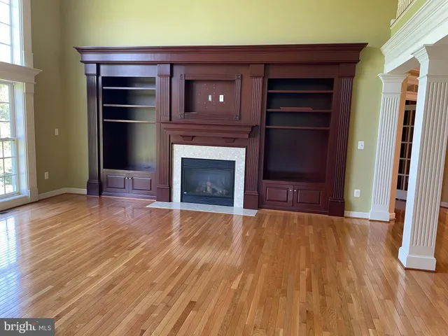 a view of an empty room with wooden floor fireplace and a window