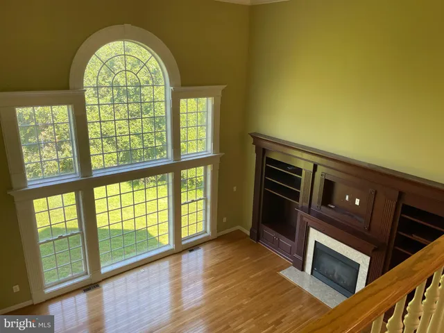 a view of an empty room with wooden floor a fireplace and a window