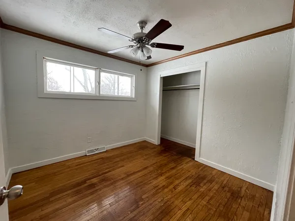 an empty room with wooden floor fan and windows