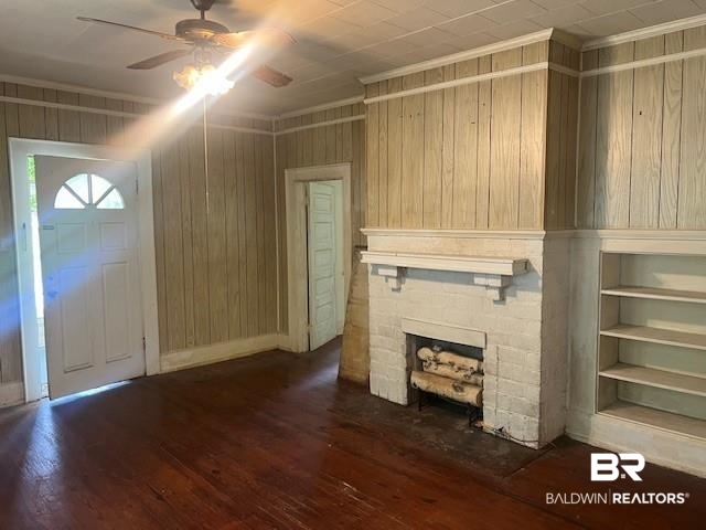 321 Grant Street Chickasaw, AL 36611 - Photo 7 of 13 Unfurnished living room featuring a ceiling fan, hardwood / wood-style floors, wooden walls, a stone fireplace, and crown molding