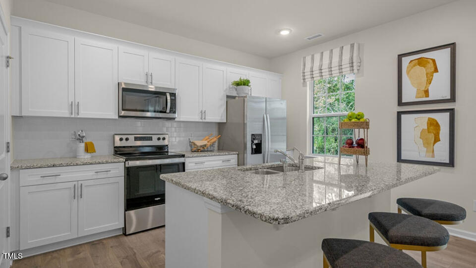 1256 Pavo Path Wendell, NC 27591 - Photo 4 of 30 a kitchen with stainless steel appliances granite countertop a sink dishwasher stove and microwave with wooden floor