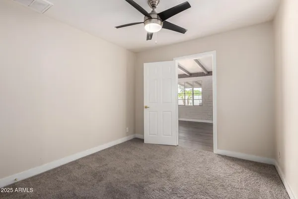 an empty room with chandelier fan and windows