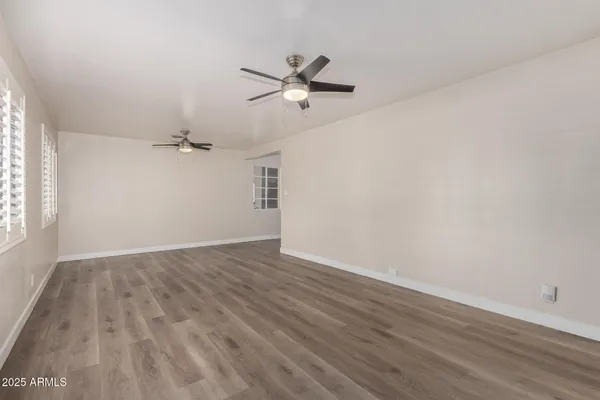 an empty room with wooden floor a ceiling fan and windows
