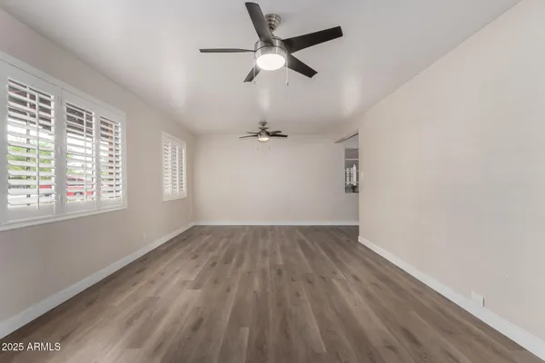an empty room with wooden floor ceiling fan and windows