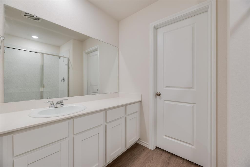3407 Rendezvous Way Sherman, TX 75090 - Photo 14 of 17 Bathroom featuring a white vanity with a single basin sink, an expansive wall-mounted mirror, wood-finish flooring, and a glass-enclosed shower with a sliding door