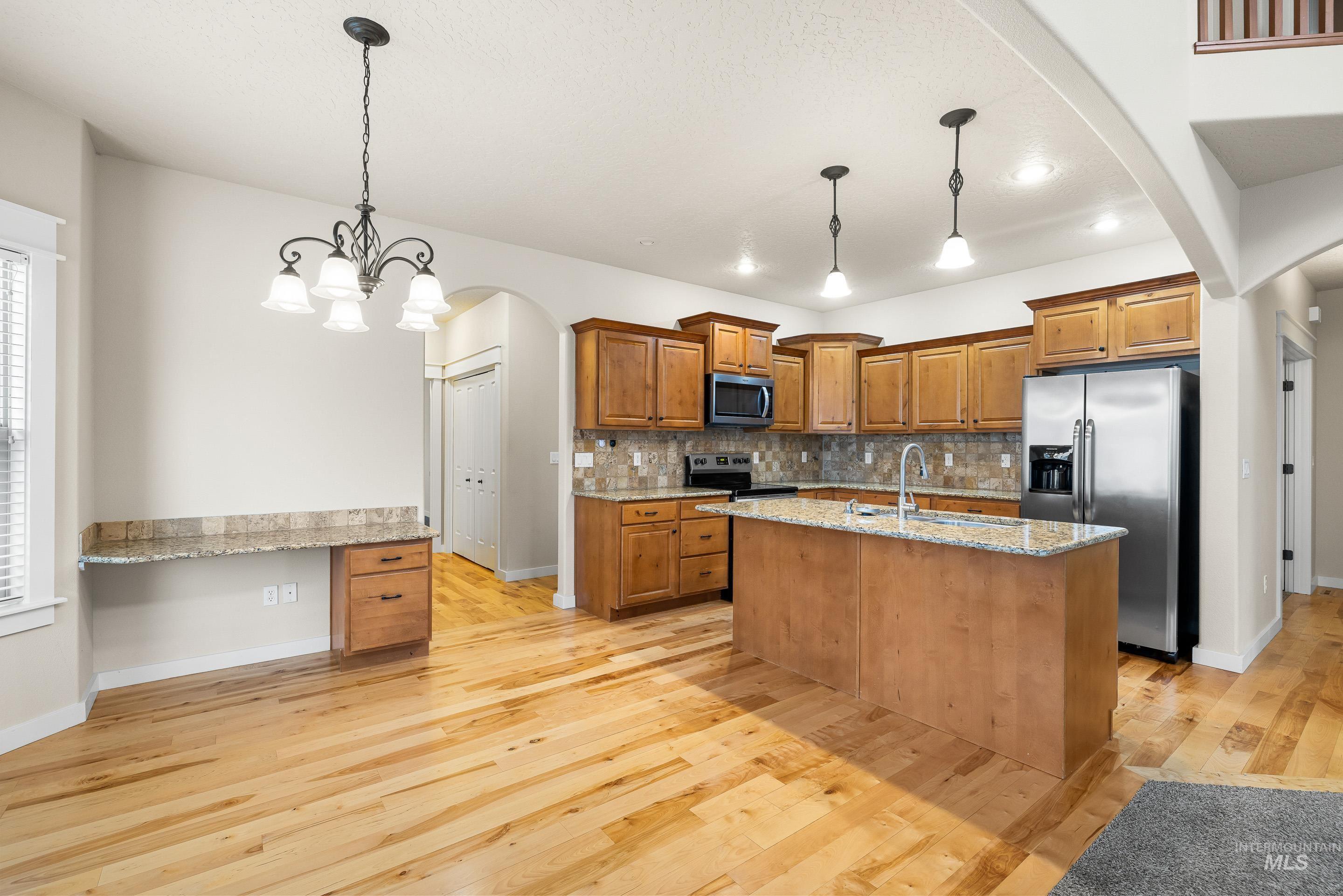 2578 South Groom Way Meridian, ID 83642 - Photo 10 of 39 Kitchen with arched walkways, brown cabinetry, stainless steel appliances, a center island with sink, and hanging light fixtures