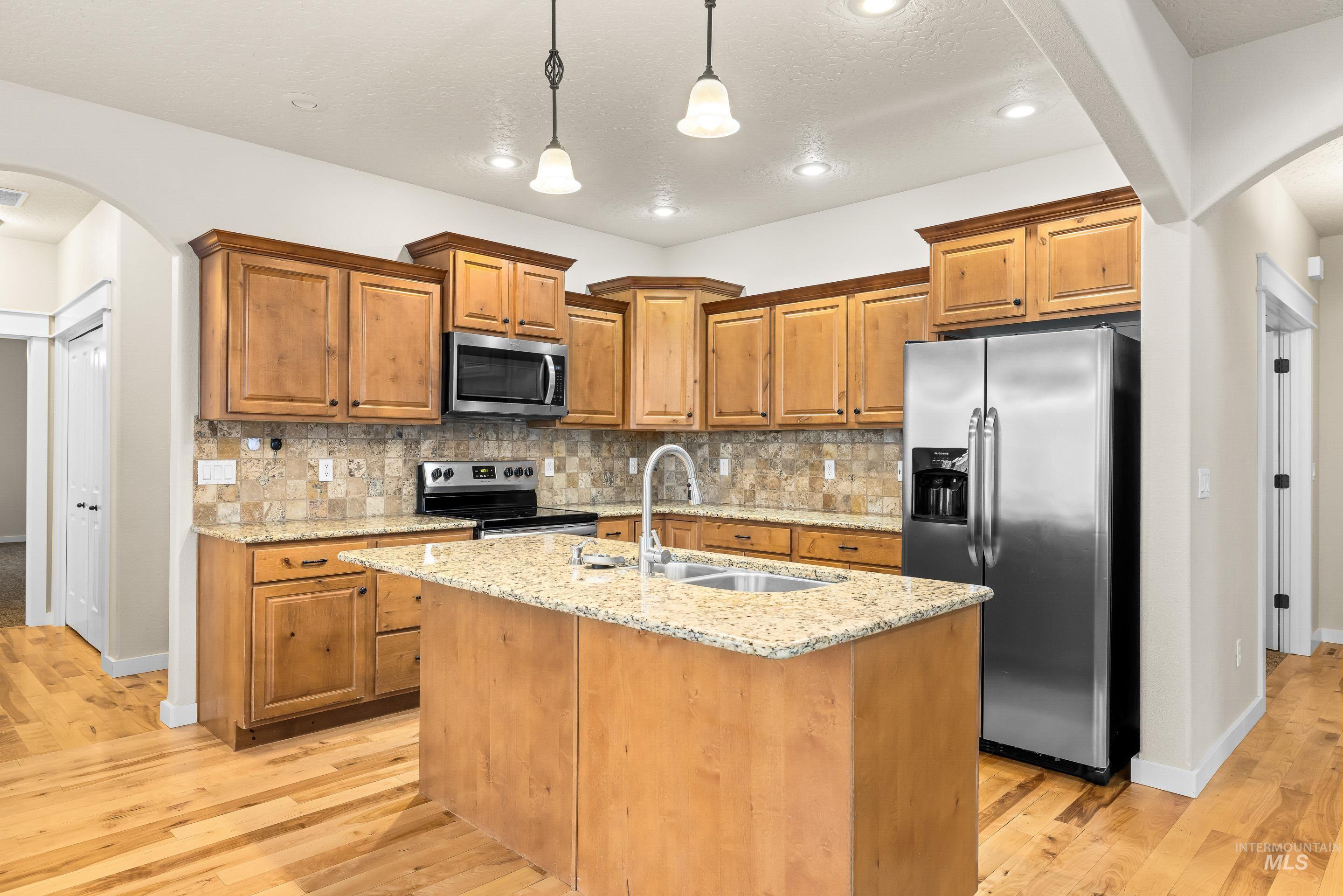 2578 South Groom Way Meridian, ID 83642 - Photo 11 of 39 Kitchen with arched walkways, light stone counters, stainless steel appliances, brown cabinets, and recessed lighting