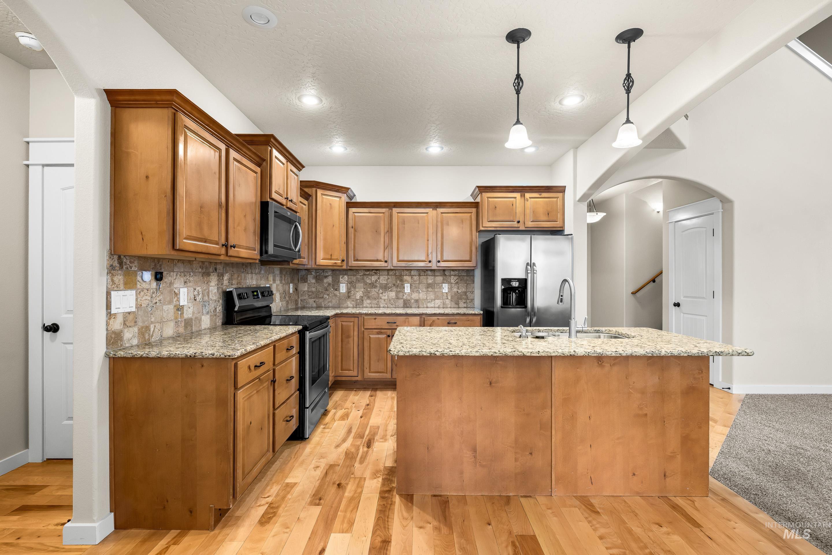 2578 South Groom Way Meridian, ID 83642 - Photo 12 of 39 Kitchen featuring arched walkways, brown cabinets, appliances with stainless steel finishes, light stone counters, and hanging light fixtures