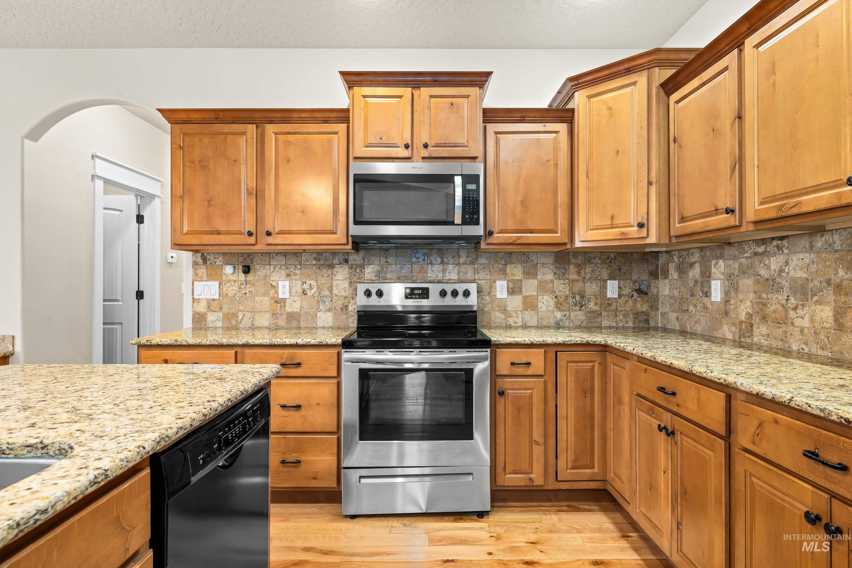 2578 South Groom Way Meridian, ID 83642 - Photo 15 of 39 Kitchen featuring appliances with stainless steel finishes, brown cabinets, light stone countertops, light wood-style flooring, and tasteful backsplash