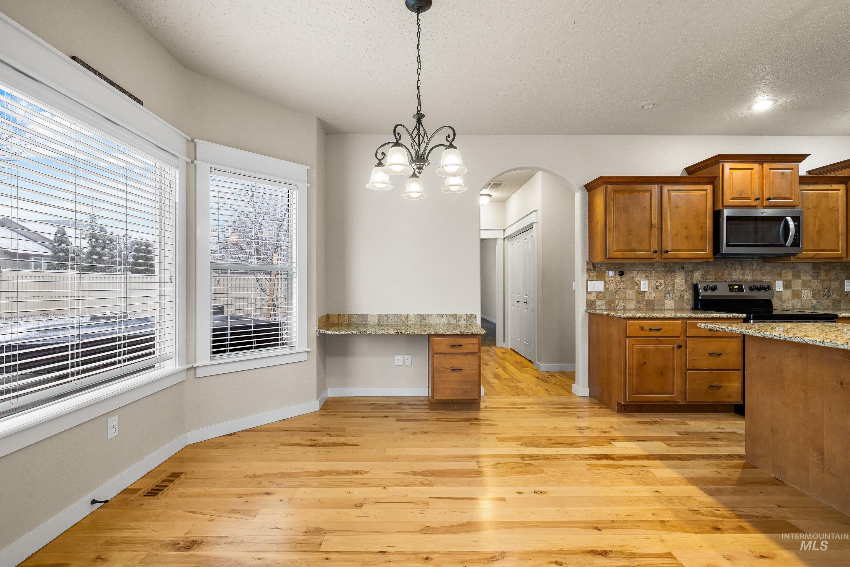 2578 South Groom Way Meridian, ID 83642 - Photo 7 of 39 Kitchen with brown cabinetry, arched walkways, light stone countertops, hanging light fixtures, and stainless steel appliances