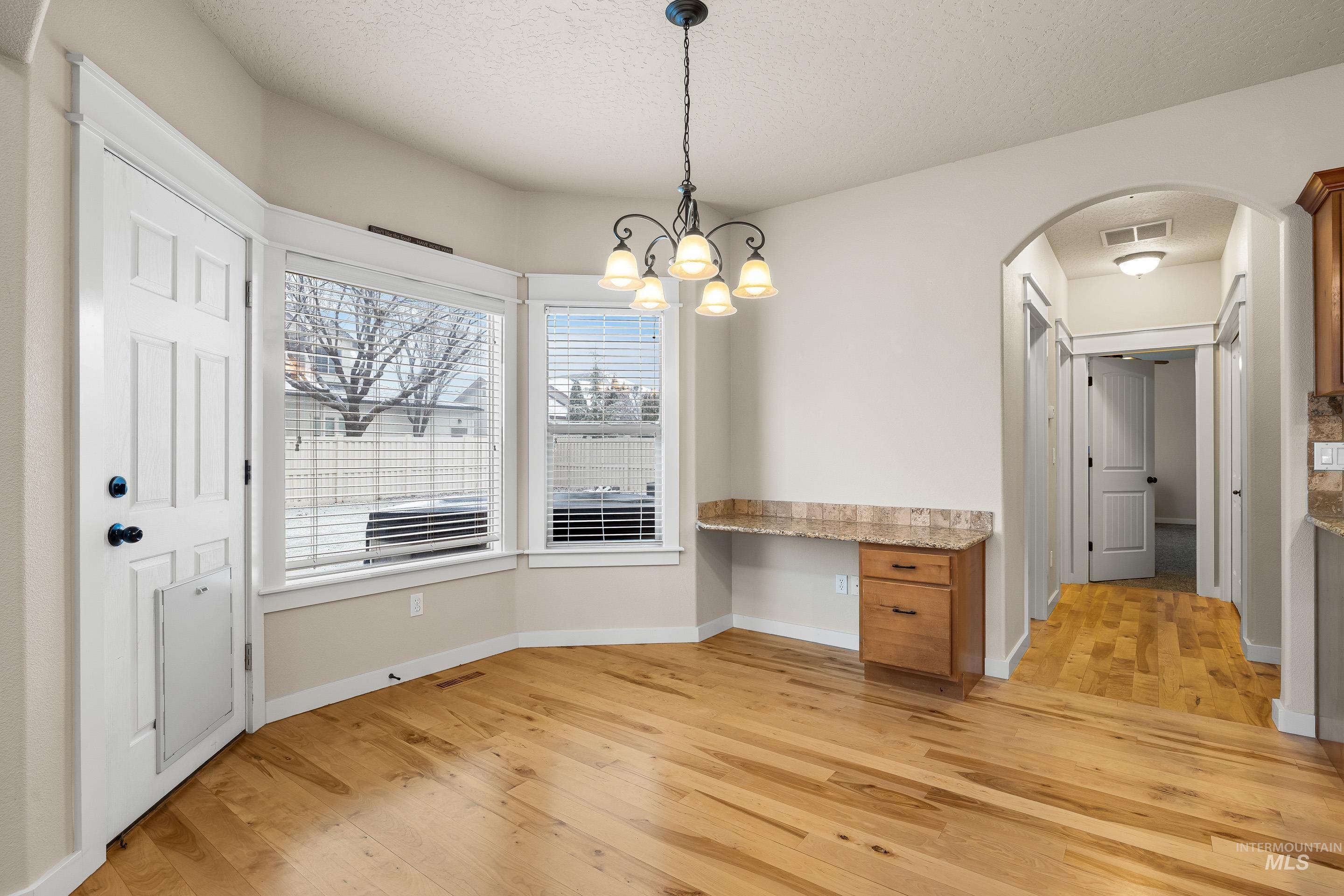 2578 South Groom Way Meridian, ID 83642 - Photo 9 of 39 Unfurnished dining area with arched walkways, light wood finished floors, a textured ceiling, a chandelier, and a desk