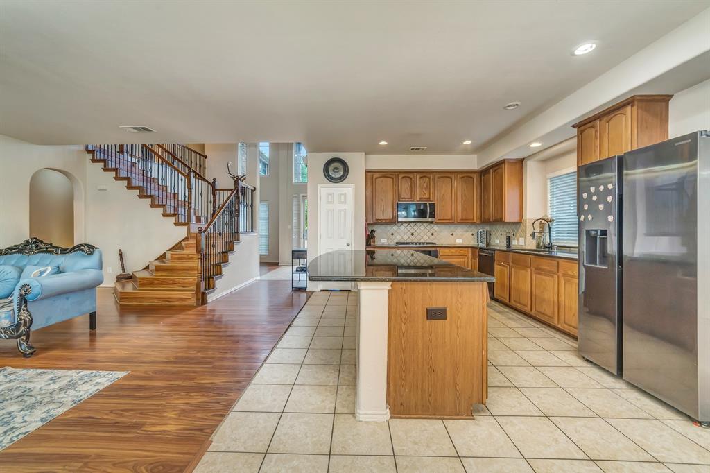 2312 Tawny Owl Road Grand Prairie, TX 75052 - Photo 17 of 40 Kitchen with black refrigerator with ice dispenser, light tile patterned flooring, dark stone counters, a kitchen island, and wood finish cabinets